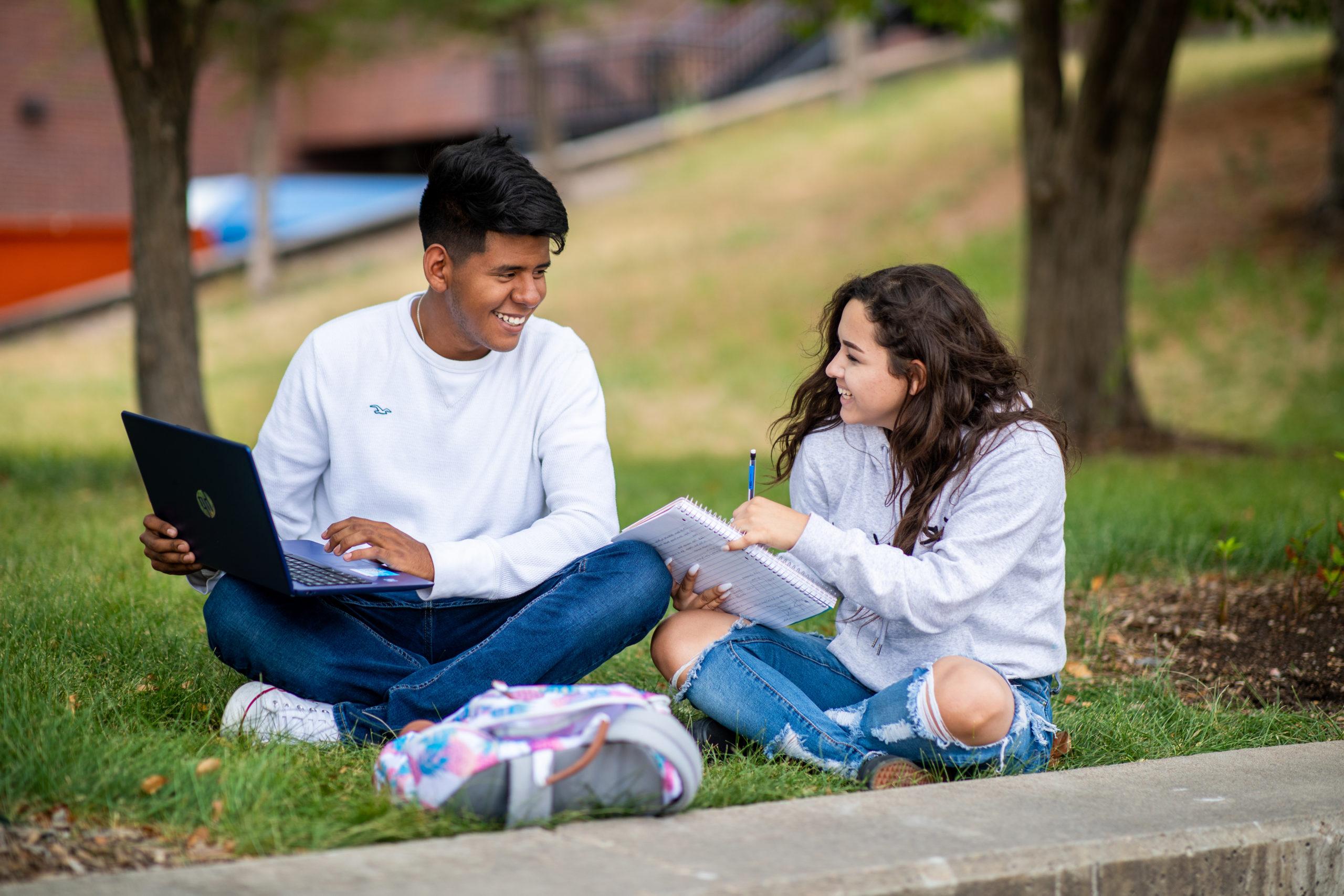 Two people sitting outside on a grassy lawn area studying together