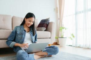 Asian girl wearing jeans using a laptop while sitting on the floor at home. Freelance girls are video conferencing with colleagues on social media. concepts work from home and new normal